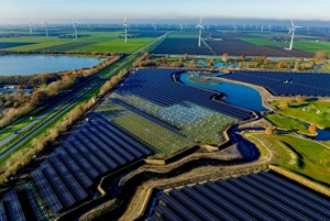 Aerial view of a sprawling solar farm alongside wind turbines in a green landscape