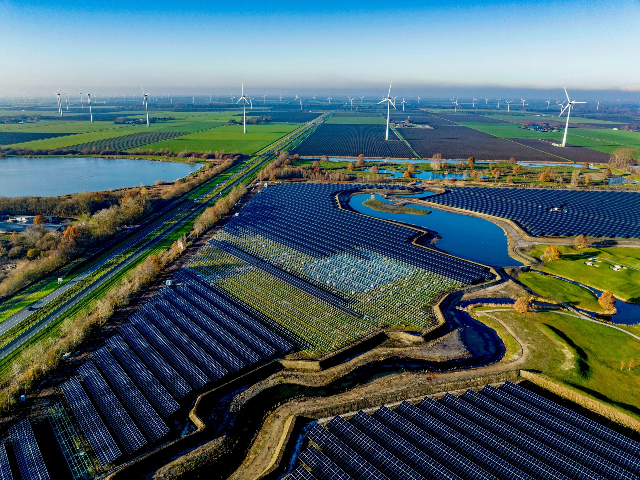 Aerial view of a sprawling solar farm alongside wind turbines in a green landscape