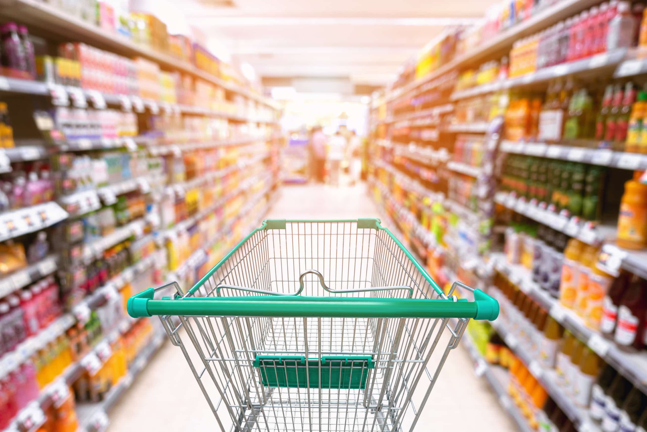 An empty grocery cart in the middle of a grocery store aisle.