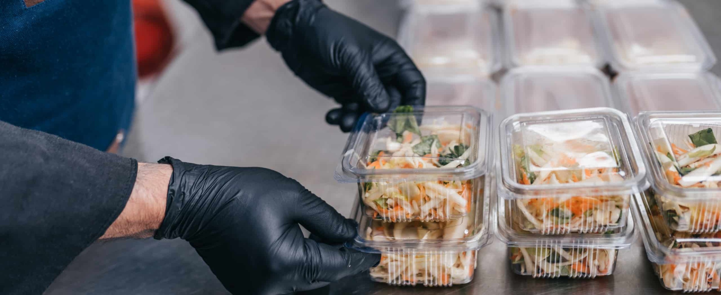 Food being packed in clear, disposable food packages.