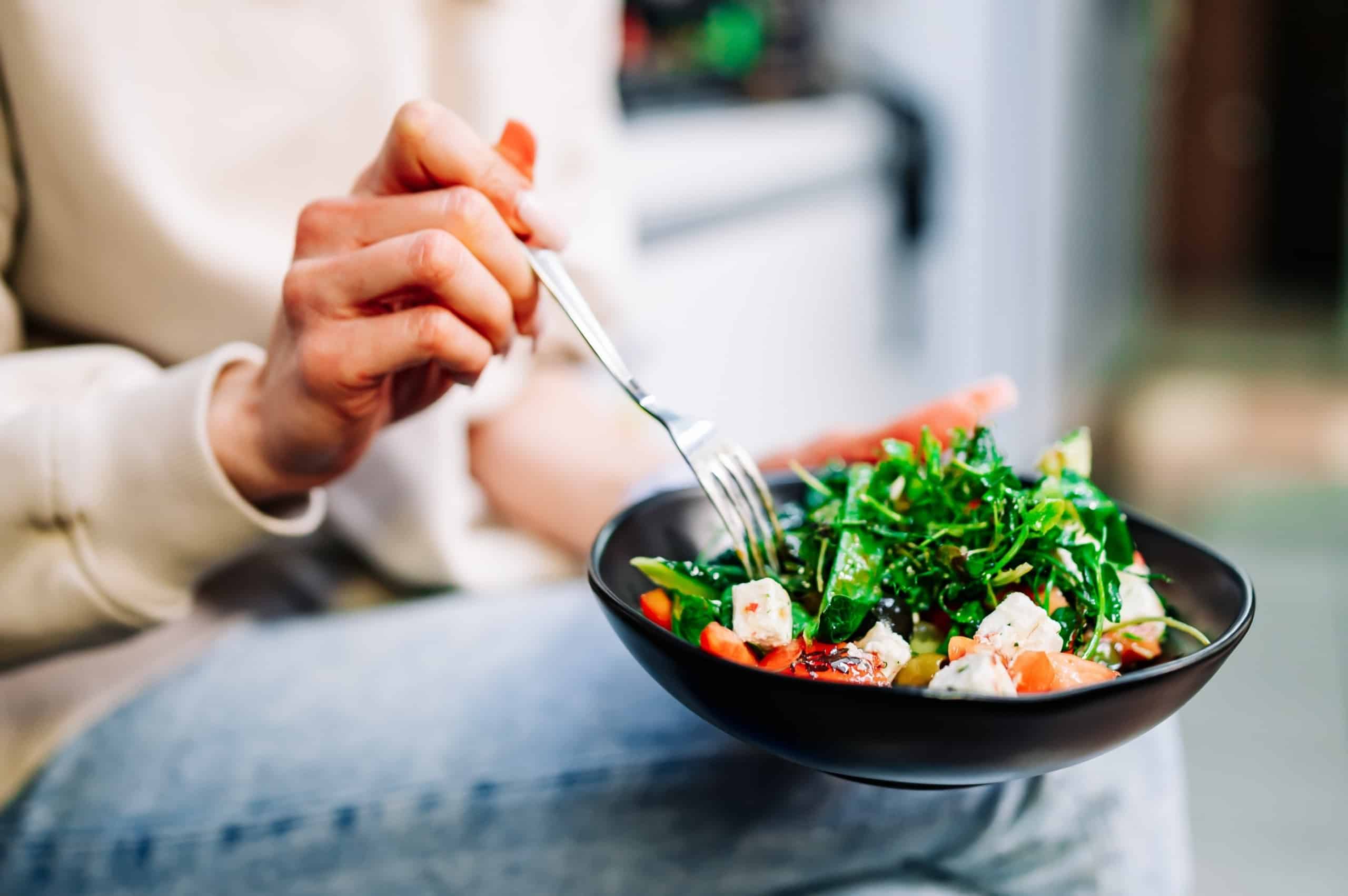Woman eating a salad with cheese, vegetables, and tofu